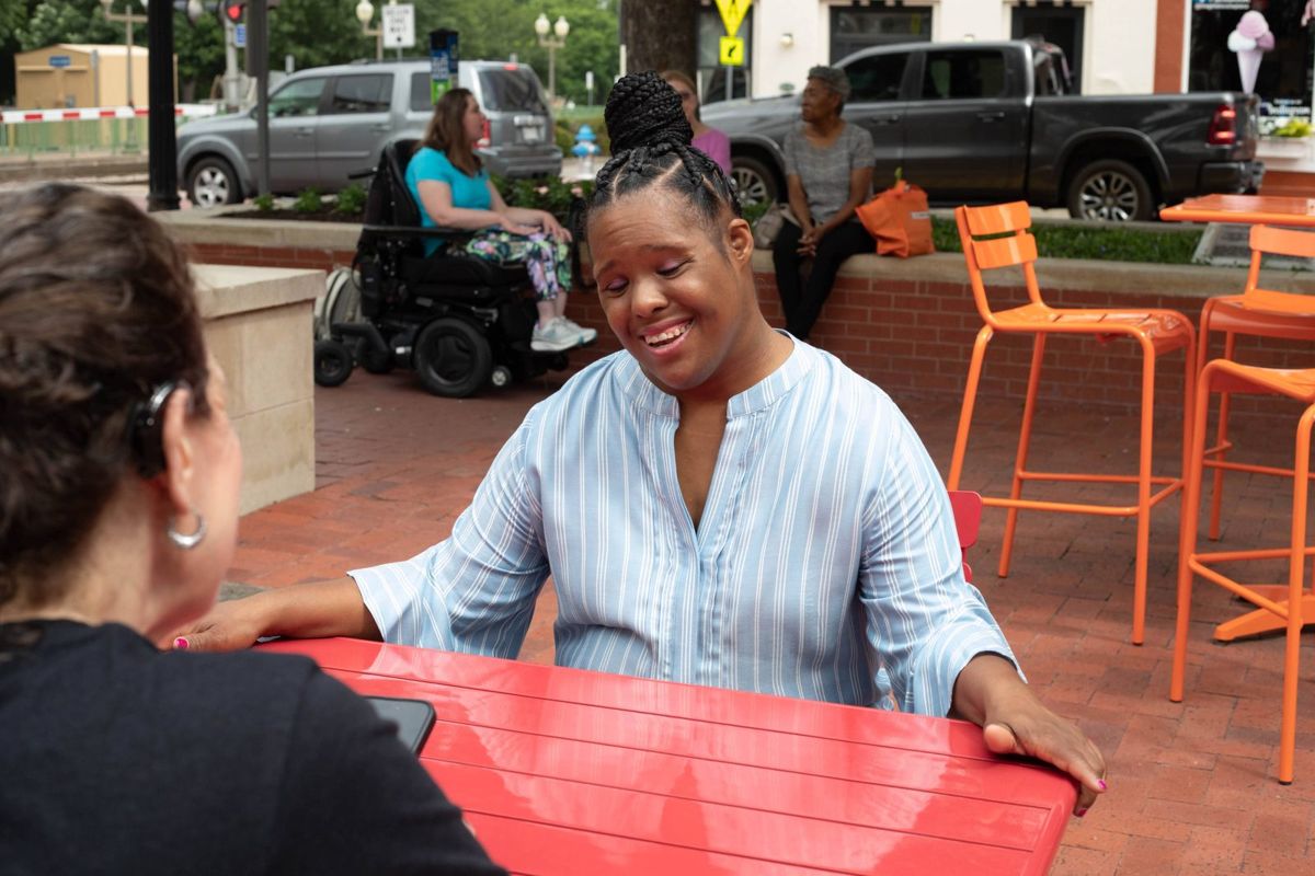 A woman laughs while talking with a friend at an outdoor table.