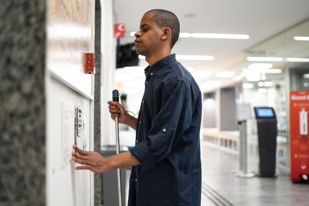 A man with a white cane walks through an office hallway.