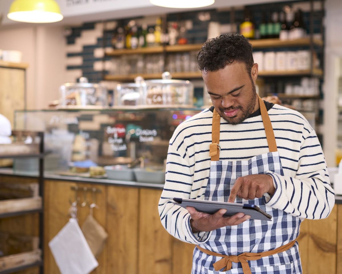 A man in an apron checks a tablet in a bakery.
